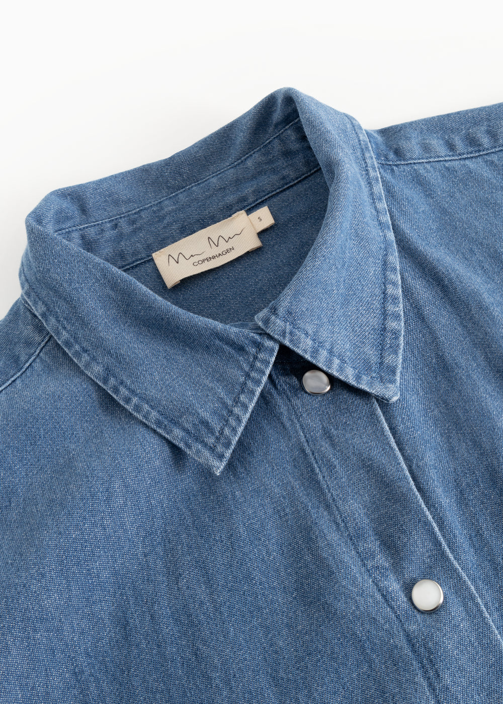 Detalje af blå denimskjorte: krave, knapper og inderside med mærketape