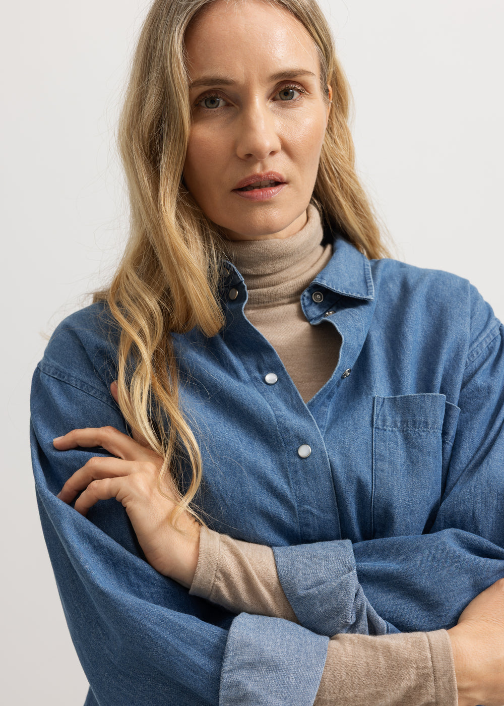 Model i blå denimskjorte med knaplukning og brystlomme, lange ærmer og krave