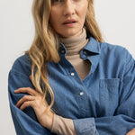 Model i blå denimskjorte med knaplukning og brystlomme, lange ærmer og krave