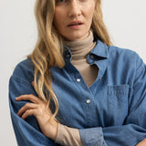 Model i blå denimskjorte med knaplukning og brystlomme, lange ærmer og krave