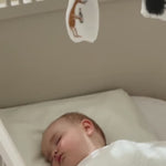 Baby sover i tremmeseng under hvidt tæppe med Moomin uro over