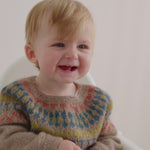 Smilende baby iført beige uldstrikbluse med mønster